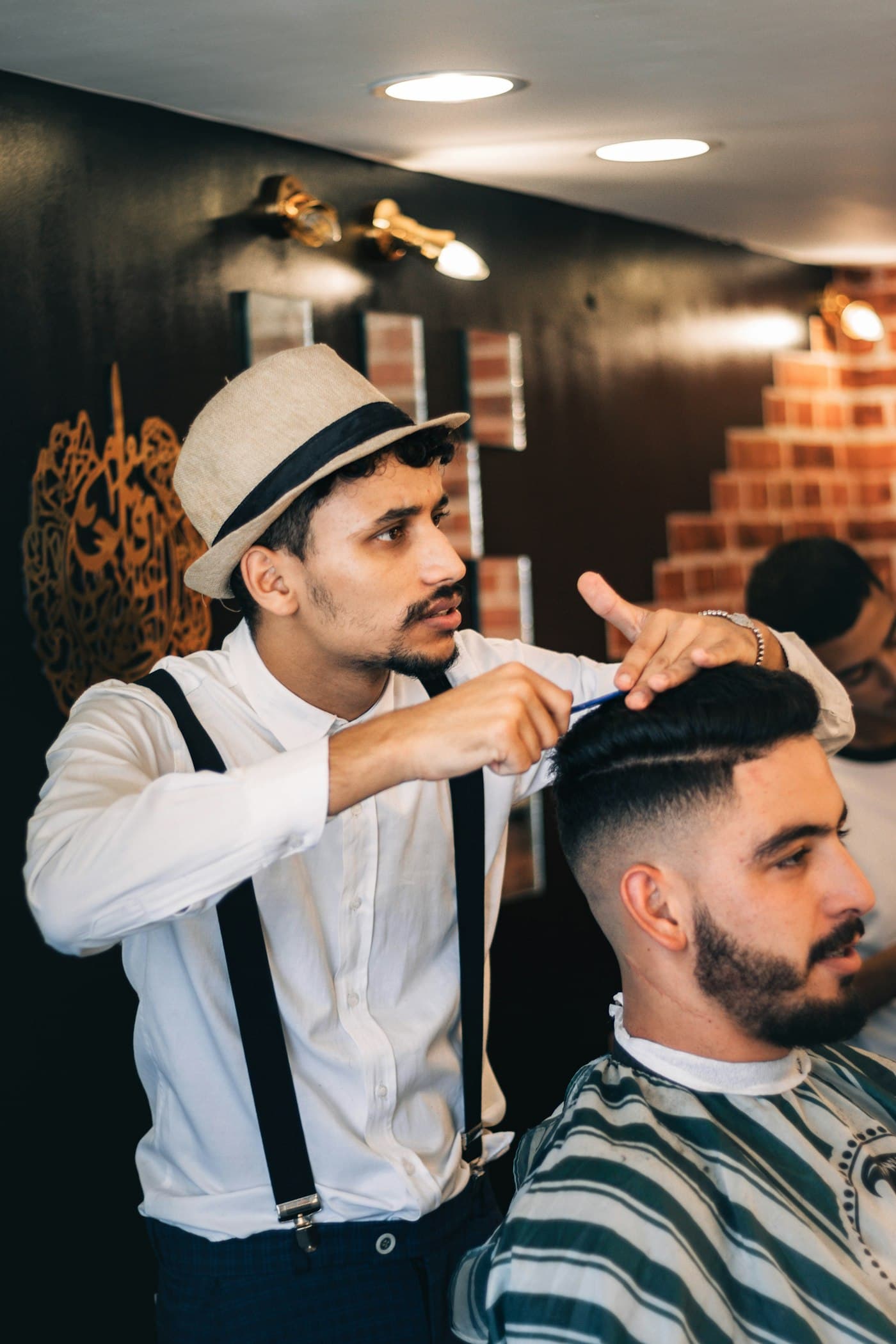 Barbier mit Strohhut und Hosenträgern stylt den Fade eines Kunden