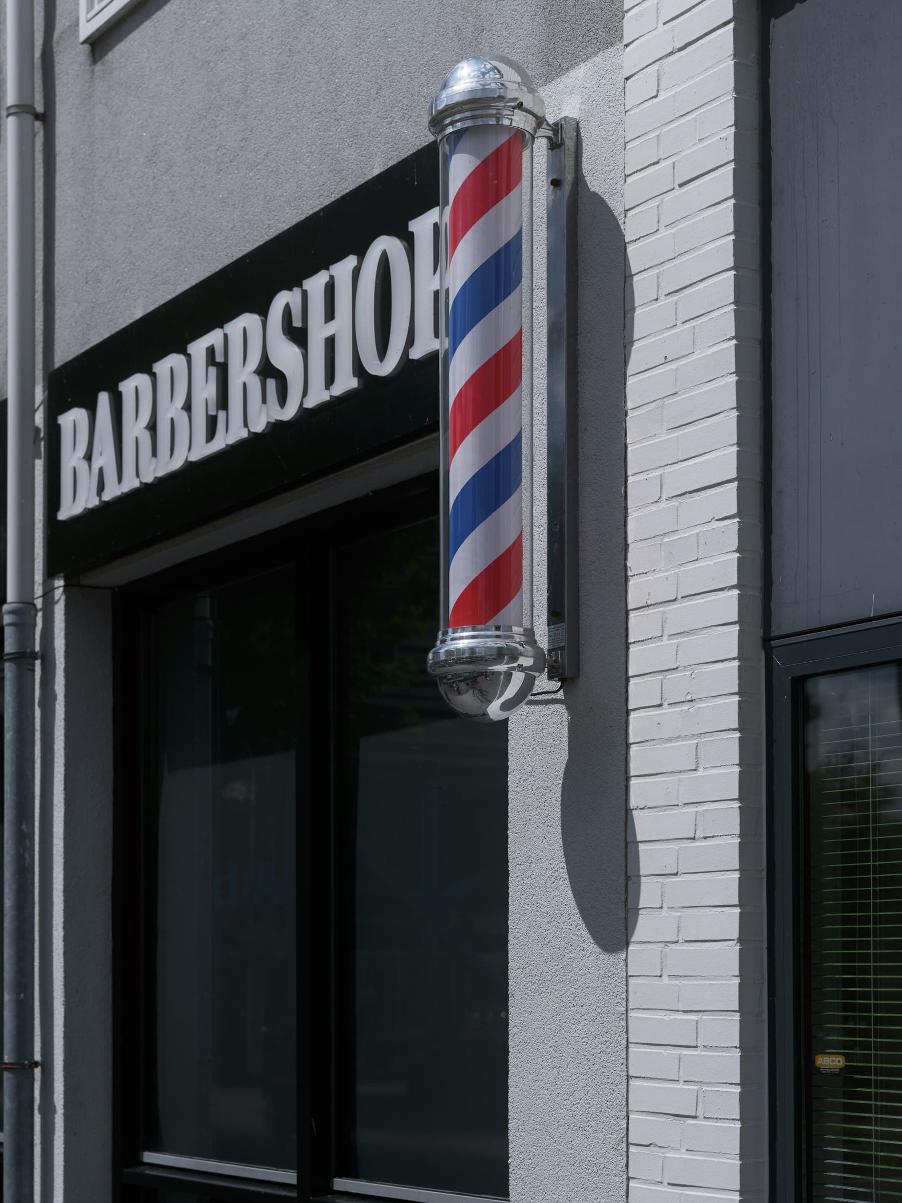 Unser Ladenschild und die rot-weiß-blaue Barber Pole neben der Tür
