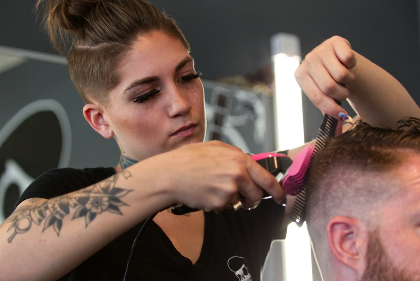 Elif schneidet einem Kunden mit Schere und Kamm die Haare